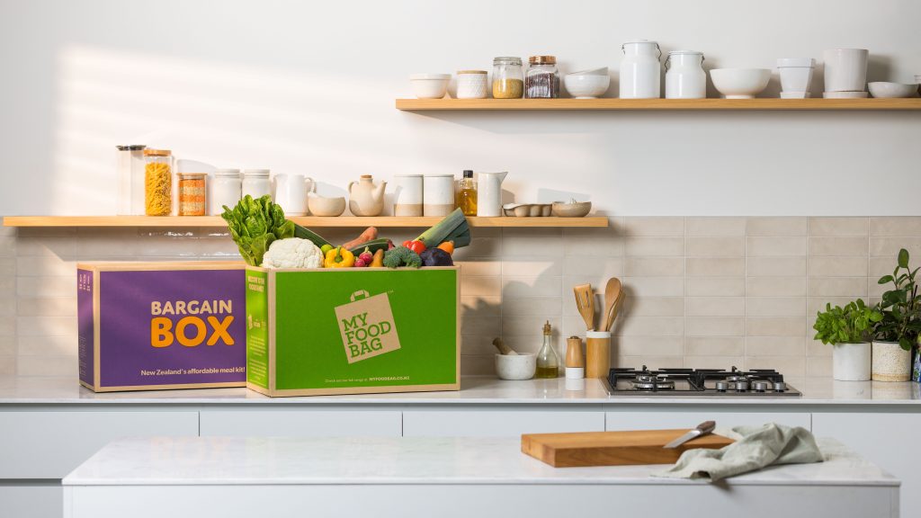 A Bargain Box and My Food Bag meal kit filled with fresh produce sitting on a kitchen bench